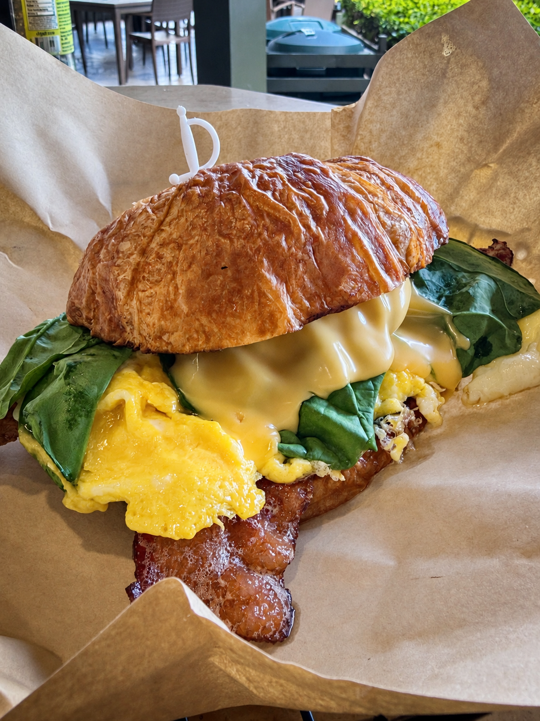 Early Bird Breakfast Sammie on a flaky croissant with eggs, greens, cheese, and bacon